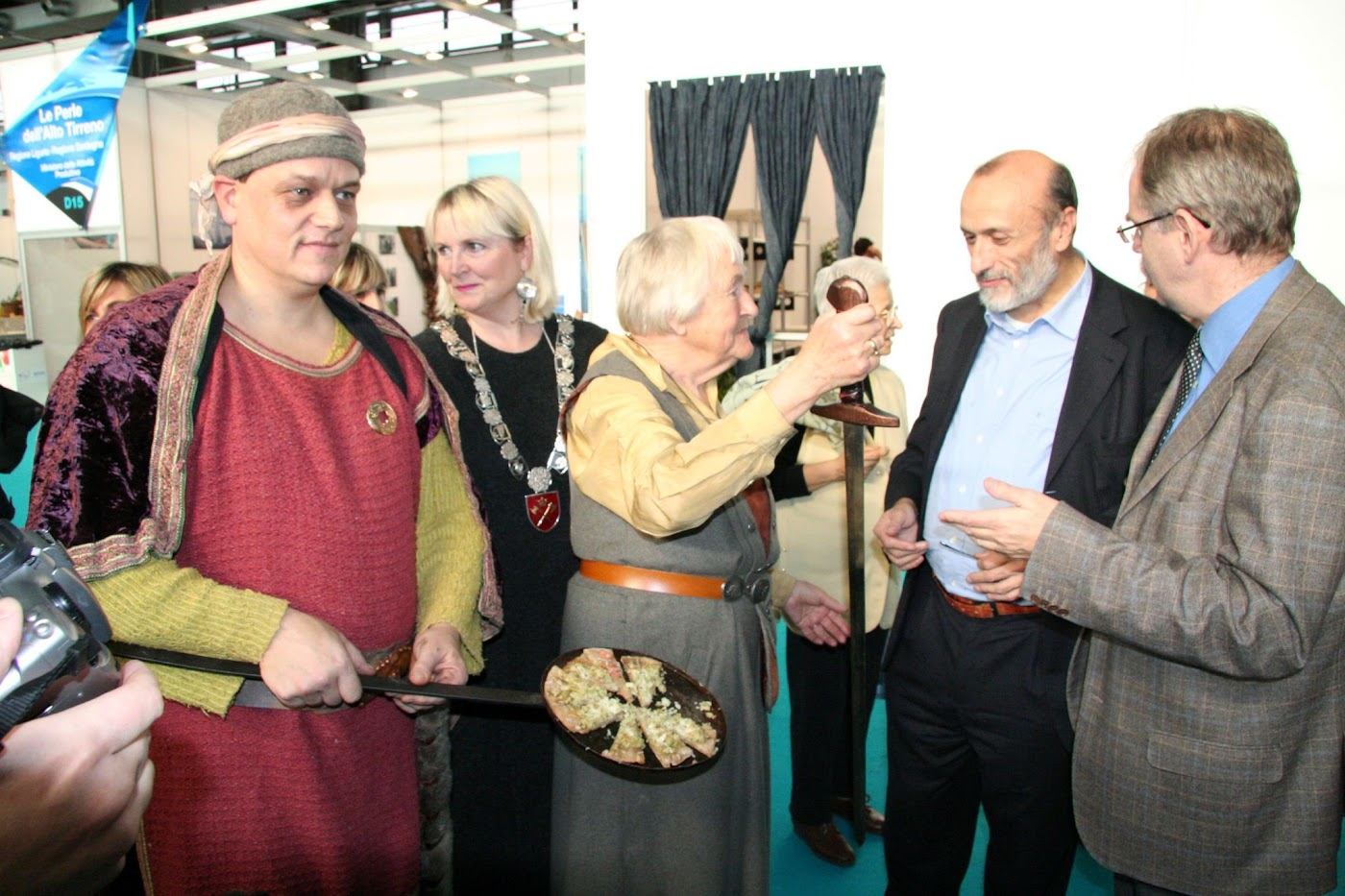 Astri Riddervold rekker fram en langskaftet panne med oppdelt vikingpizza til Carlo Petrini på messestanden, omgitt av norske gjester