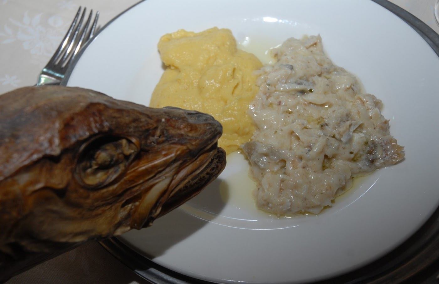 Tallerken med utvannet tørrfisk i hvit saus og gul polenta, med et tørket torskehode liggende inntil tallerkenkanten
